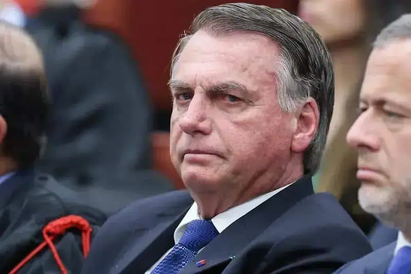 Homem de terno e gravata com expressão séria em ambiente formal, possivelmente em evento jurídico ou político.