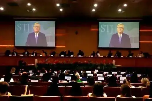 Profissionais em conferência de direito, com a tela exibindo um convidado e o público atento ao evento jurídico.