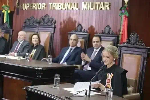 Julgamento no Superior Tribunal Militar com ministros e advogada apresentando defesa, em ambiente formal com decoração de madeira e escudos do tribunal.
