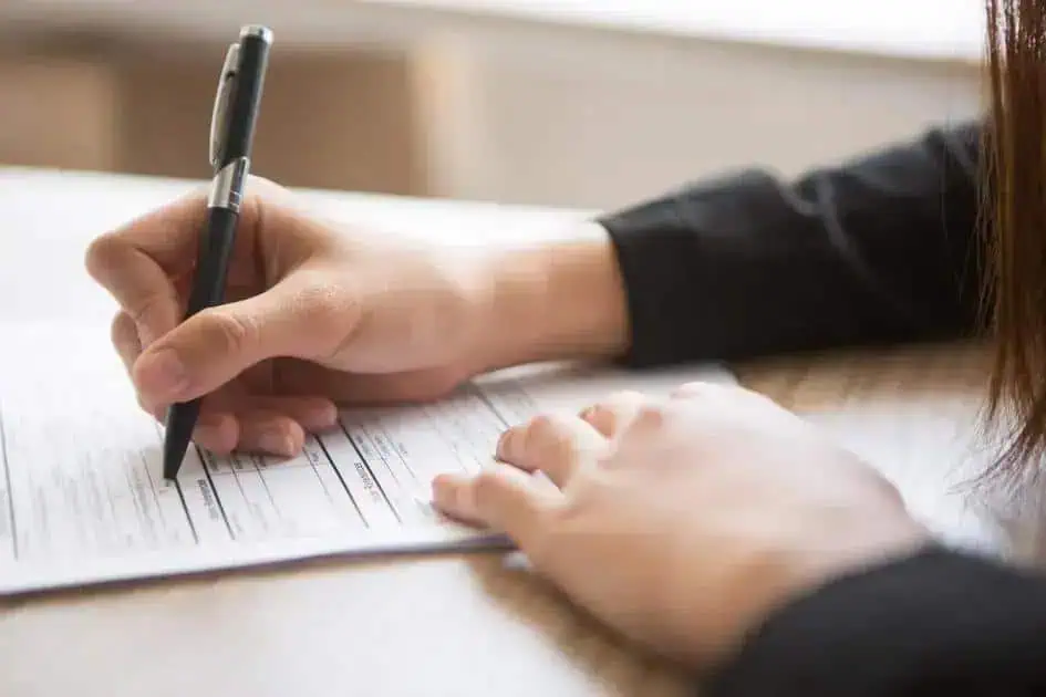 A3. Pessoa assinando documento importante relacionado ao direito, advocacia, justiça ou noticias jurídicas, em ambiente de escritório ou tribunal.
