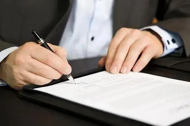 Homem assinando documento oficial em ambiente de escritório, representando ações jurídicas e direitos legais.