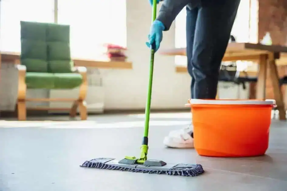 Limpeza doméstica profissional sendo realizada com esfregão e balde de água em ambiente de escritório.