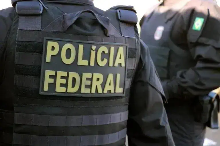 Polícia Federal em operação policial, destaque para policial de uniforme preto com badge.