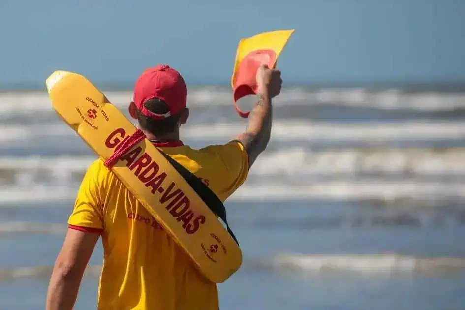 Homem usando colete e boné na praia, simbolizando proteção e segurança jurídica, relacionado a direitos e proteção ao cidadão, com foco em notícias de direito e legislação.