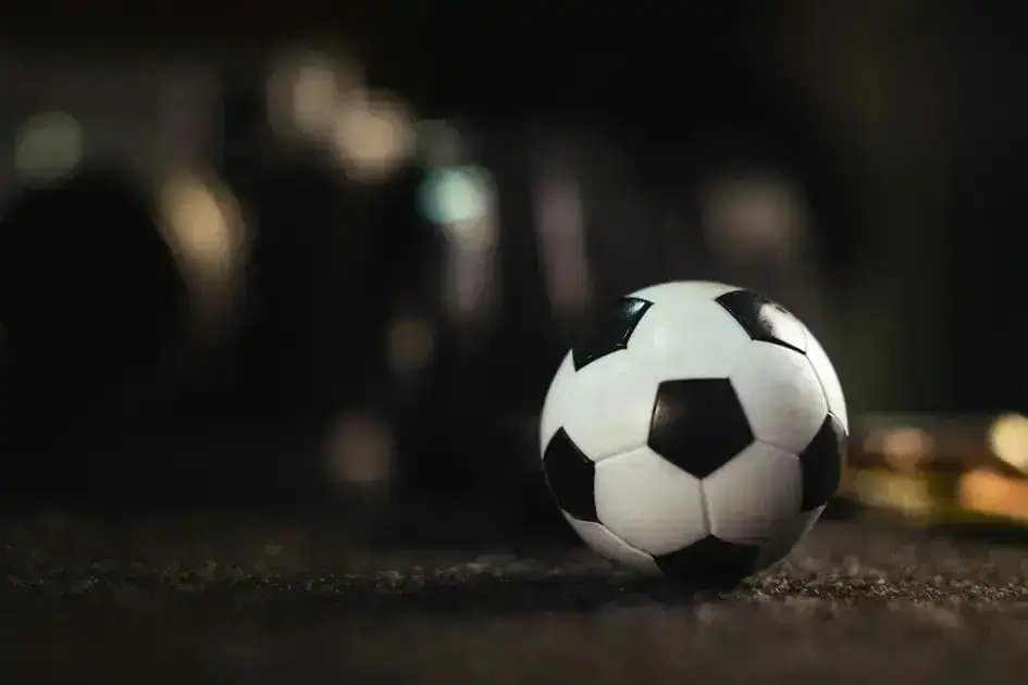 Bola de futebol em destaque na imagem, com fundo escuro e iluminação suave, representando esportes e jogos.