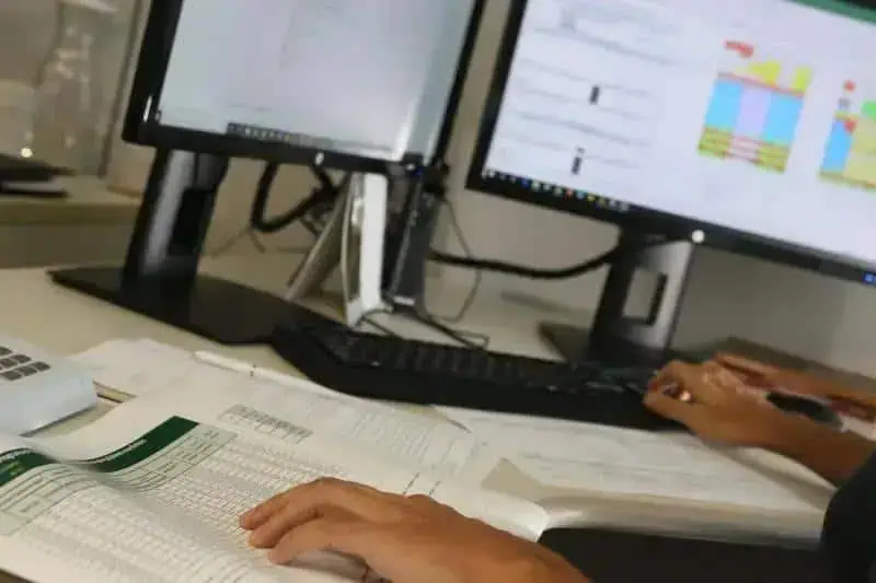 Relatório de análise jurídica sendo realizado em escritório de advocacia com computadores e documentos.