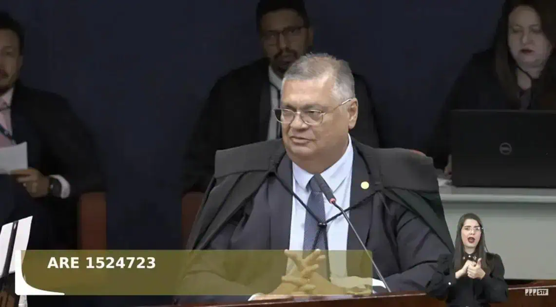 Advogado em tribunal durante sessão de julgamento de caso de direito, com outros profissionais ao fundo.
