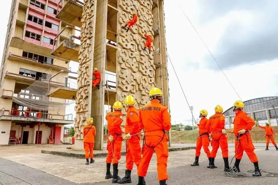 Resgate de altura com bombeiros em treinamento numa fachada de prédio em construção, demonstrando procedimentos de segurança e atuação em situações de emergência.