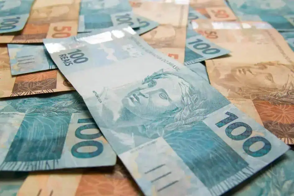 100 reais em cédulas de dinheiro brasileiro sobre fundo de notas de diversos valores, conceito de dinheiro, economia e finanças.