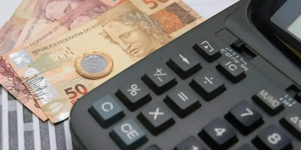 Cédula de moedas de real e cédula de contas com calculadora em fundo de linhas, símbolo de economia e finanças no contexto de notícias e direito financeiro.