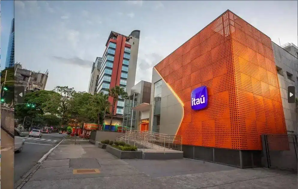 Banco Itaú na cidade com destaque para sua fachada moderna e fachada laranja vibrante, representando inovação e segurança nos serviços financeiros, no centro de uma área urbana movimentada.