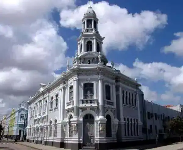 Palácio histórico de construção branca com detalhes arquitetônicos clássicos, sob céu azul com nuvens, representando patrimônio cultural e arquitetura emblemática para notícias de direito e história.