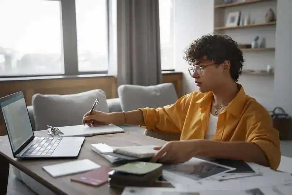 Estudante estudando direito em casa, com laptop, livros e materiais de estudo, simbolizando pesquisa e preparação jurídica.