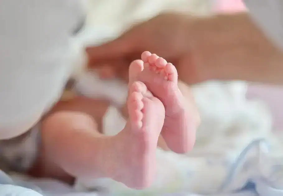 Recém-nascido nos braços da mãe com foco em seus pequeninos pés.