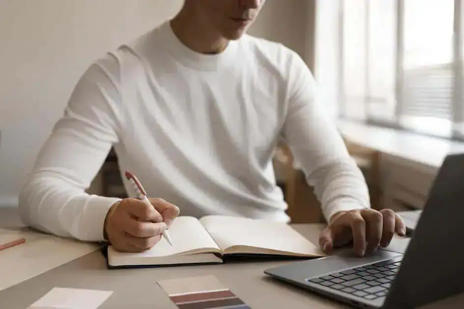 Estudante escrevendo em caderno com laptop aberto ao lado, ambiente confortável para estudo e pesquisa jurídica, foco em direitos, notícias e atualidades no contexto do Direito Hoje Notícias.