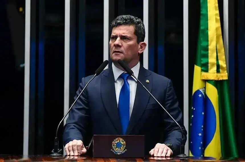 Legislador brasileiro em discurso no plenário durante sessão parlamentar, com bandeira do Brasil ao fundo, voltado para temas de direito e política no Brasil.