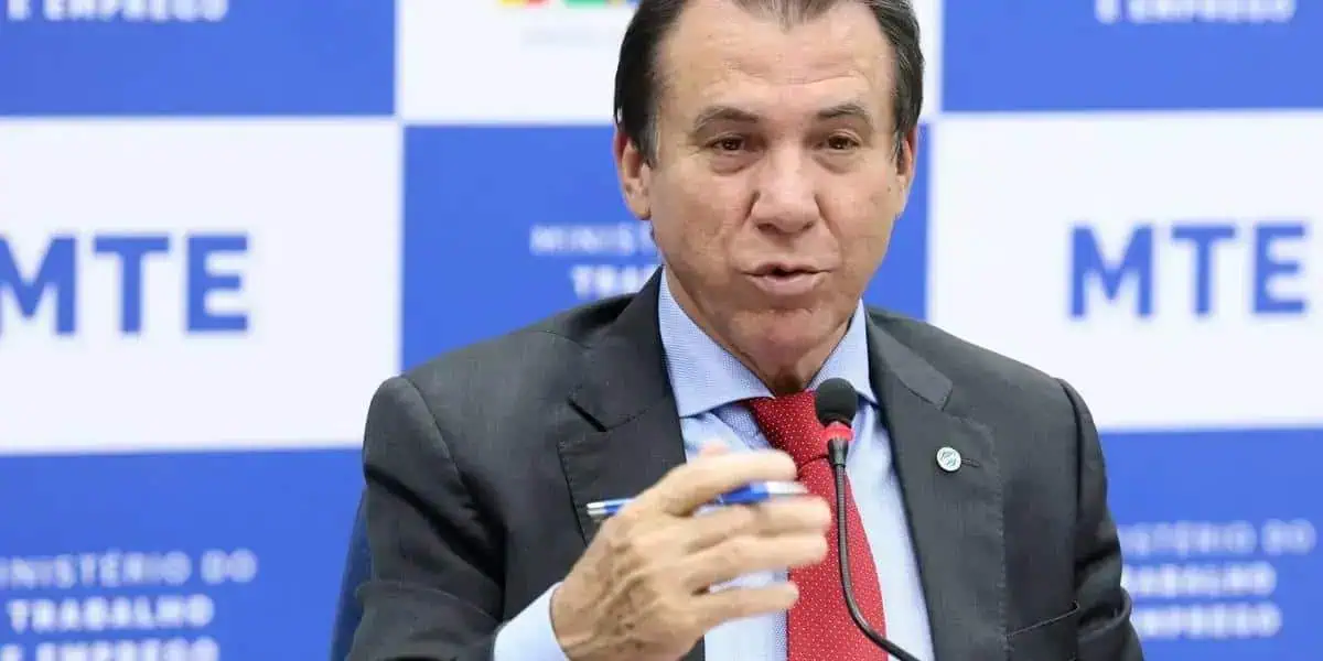 Advogado falando em evento do Ministério do Trabalho com fundo azul e logos do MTE.