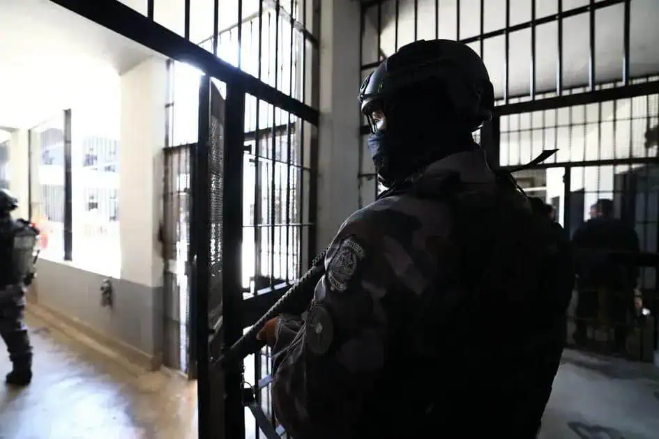 Guarda penitenciária de segurança máxima protegendo entrada de prisão durante operação policial.