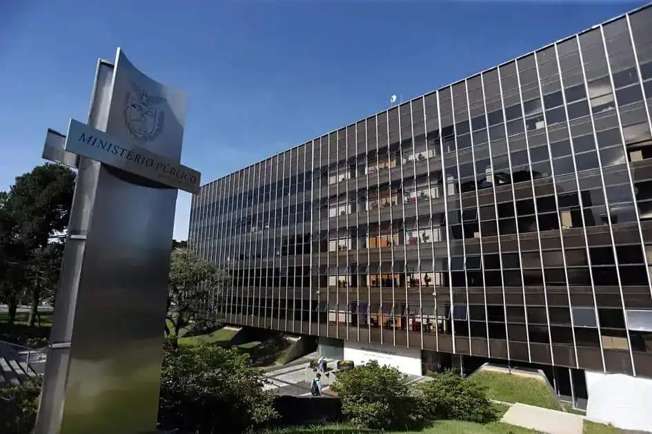 Ministério Público em frente à sede do Ministério Público, prédio moderno com fachada de vidro refletindo o céu azul, mostrando a importância da justiça e do direito no Brasil.