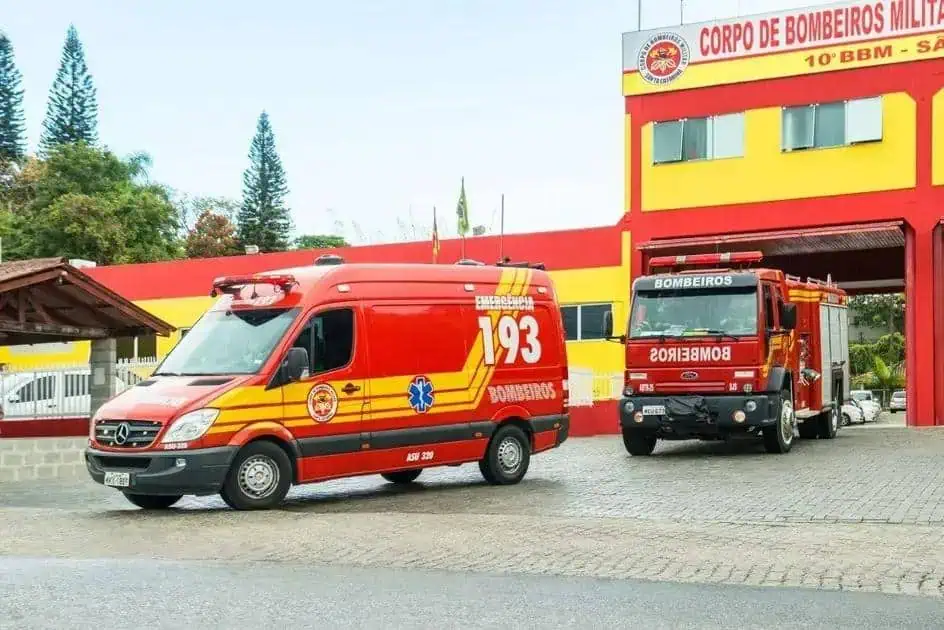 Ambulância e caminhão do corpo de bombeiros na frente da sede do corpo de bombeiros militar em destaque magenta amarelo vermelho, veículos de emergência em frente ao quartel.