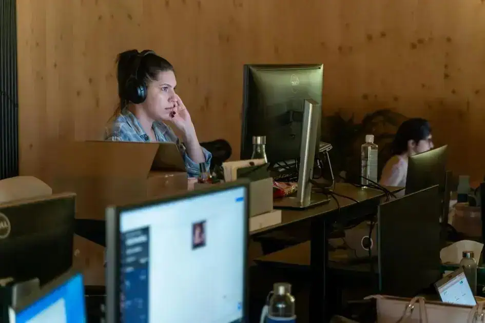 Operadora de atendimento ao cliente usando headset em ambiente de escritório com computadores e informações jurídicas, representando direitos e notícias jurídicas atuais.
