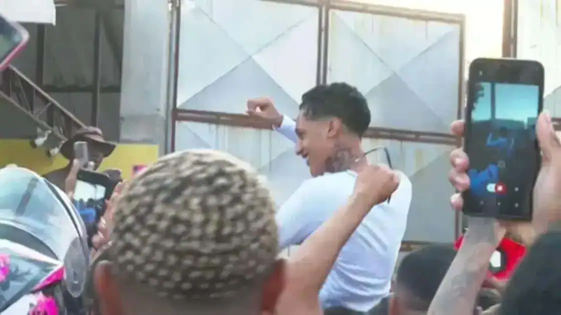 Homem celebrando vitória com alegria e apoio de pessoas ao redor, em ambiente de evento ou reunião social.
