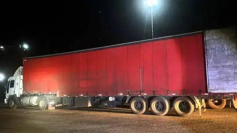 Transportadora de carga parada na estrada à noite, destacando a importância do transporte de cargas e segurança no trânsito.