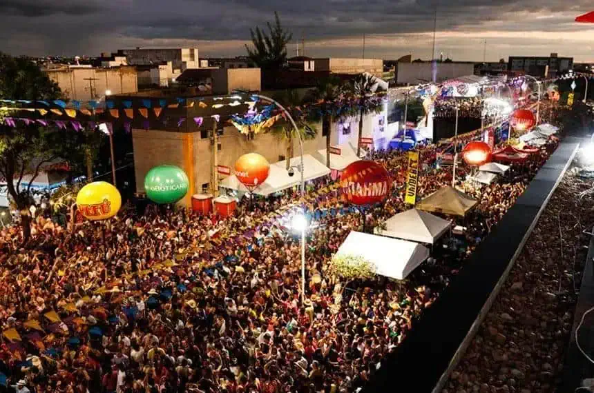 Multidão e festividades ao ar livre em evento com iluminação e balões coloridos, promovendo cultura e diversão na cidade. Evento popular com grande presença de público, música e shows em espaço urbano.