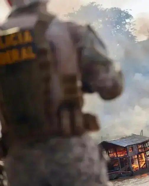 Soldado em ação durante incêndio em área urbana, com fogo e fumaça ao fundo, ilustrando uma operação de combate ao fogo ou situação de emergência, em cenário de conflito ou desastre natural.