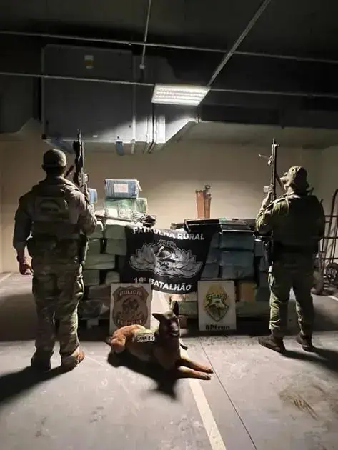 Armados policiais militares em operação com cão farejador em ambiente de garagem ou depósito, mostrando aparato policial e estratégia de combate ao crime, com foco na segurança e leis.