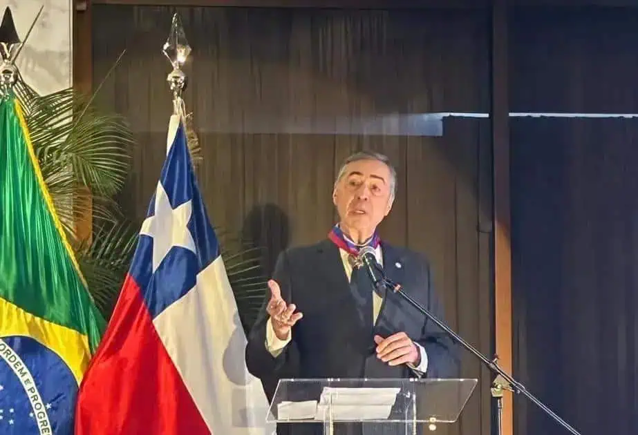 Brasileiro em discurso político ao lado das bandeiras do Brasil e Grécia, destacando temas de direito e política internacional, com foco em notícias e atualidades do Direito Hoje Notícias.