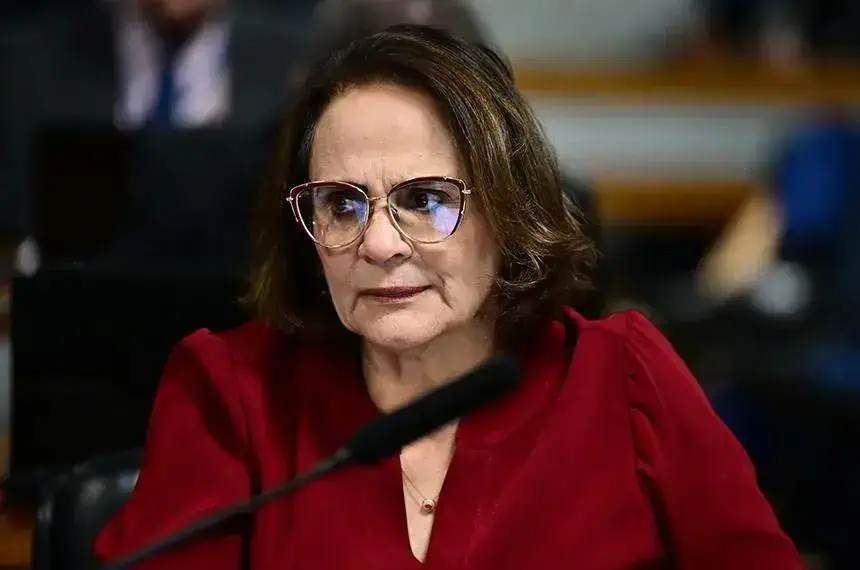 Associação de mulheres advogadas, mulher com óculos, expressão séria, em ambiente de tribunal ou reunião jurídica.