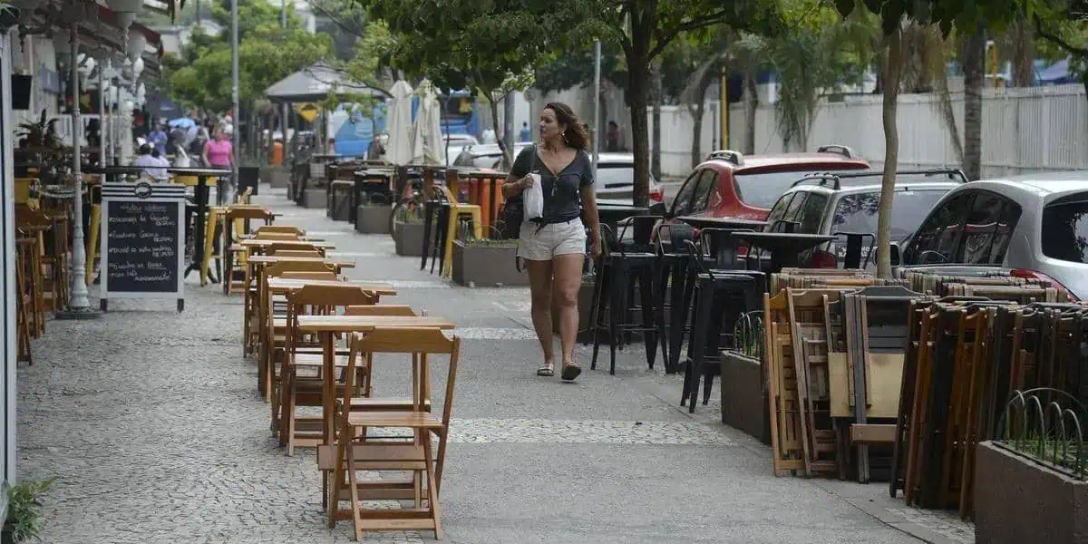 Mesma, limpos e vazios, mesas de restaurante ao ar livre na calçada de uma rua movimentada com veículos estacionados ao fundo, durante o dia.