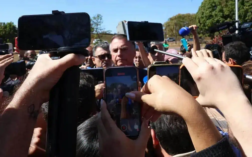 FOTO DE UMA ENTREVISTA OU EVENTO POLÍTICO, COM PESSOAS USANDO CELULARES E GRAVANDO, CENTRO DE ATENÇÃO PARA JORNALISTAS E REPÓRTERES.