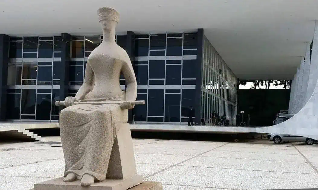 Estátua de mulher com toga e livro na frente do prédio do Supremo Tribunal Federal em Brasília, símbolo do poder judiciário e da justiça no Brasil, representando a importância do direito e do estado de direito.