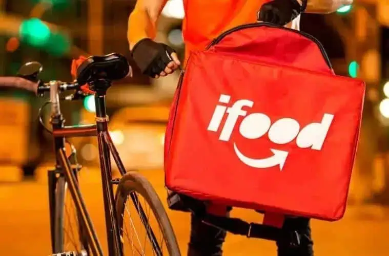 Entrega de comida rápida com bike, serviço de delivery do iFood, recorte urbano na noite, destaque para aplicativo de delivery de alimentos, transporte de pedidos de comida.