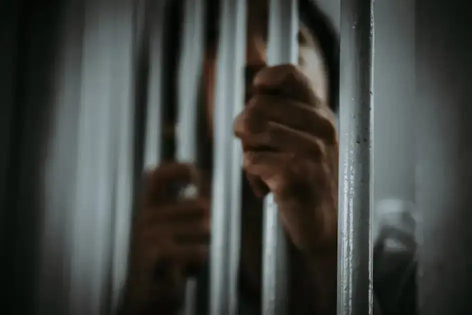 Prisão com grades de metal e mão visível em uma cela, simbolizando temas de direito penal e justiça.