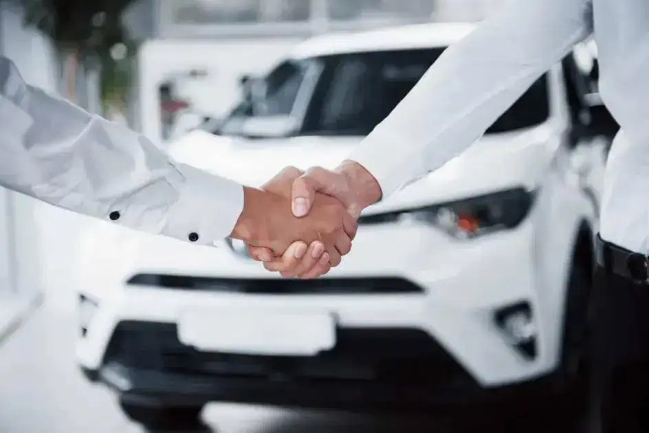 Acordo de handshake entre vendedores de carros no showroom, simbolizando negócio fechado e confiança na negociação.
