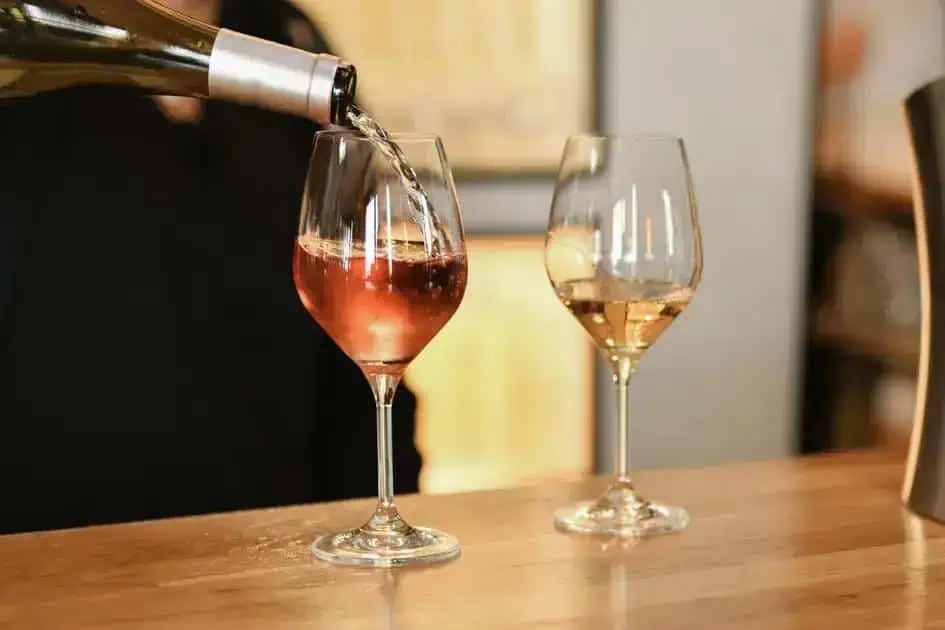 Bebida sendo servida em taça de vinho rosé, ambiente de bar, consumo de álcool, taças de vinho, Direito Hoje Notícias.