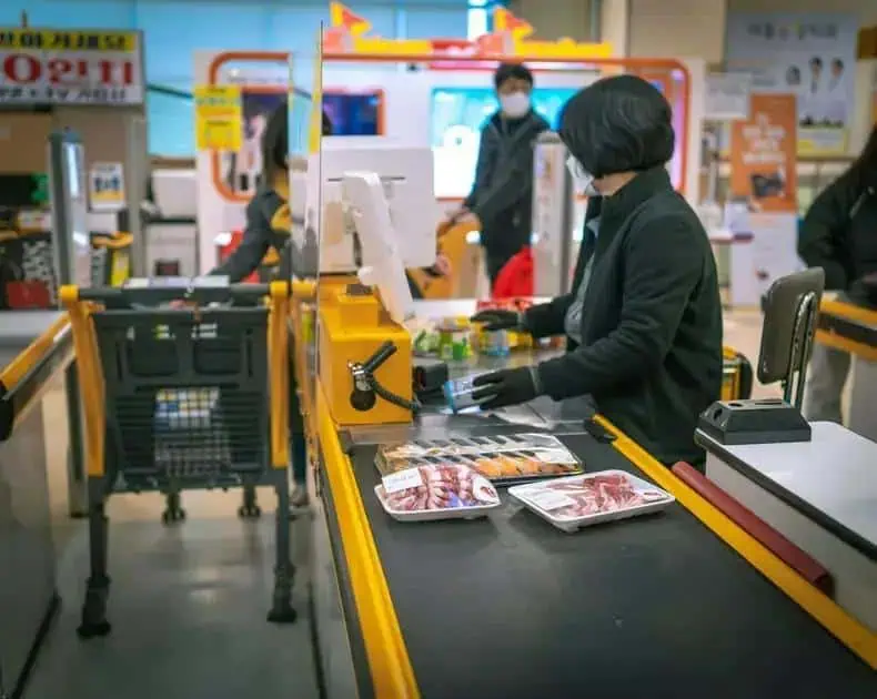 Carnê de supermercado com caixas registradoras e clientes no checkout, focando em compras de alimentos, produtos de higiene e promoções em uma loja moderna.