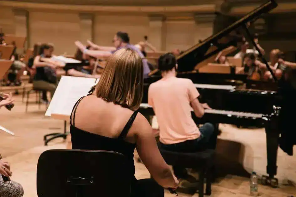 Artesãos de música clássica em ensaio orquestral com piano, violino e outros instrumentos, jovens músicos praticando em ambiente de estúdio musical.