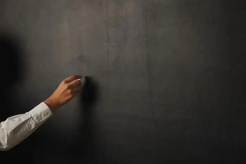 Fachada de quadro-negro com mão escrevendo com giz, símbolo de educação, escola ou aula, conceito de aprendizado e ensino, ambiente escolar, educação formal, sala de aula moderna, imagem representativa de ensino e formação profissional.