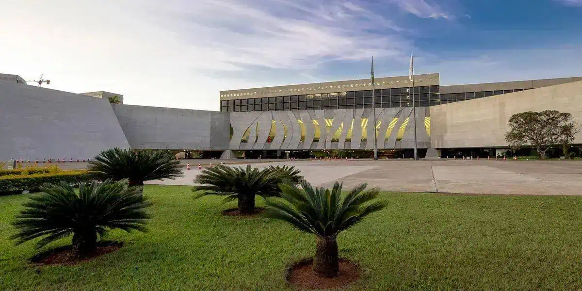 Edifício do Congresso Nacional em Brasília, sede do poder legislativo no Brasil, com jardim bem cuidado na frente e céu claro ao fundo.