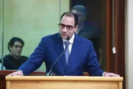 Advogado de terno azul e óculos falando em tribunal, representando o direito e a justiça em audiência judicial no Brasil.