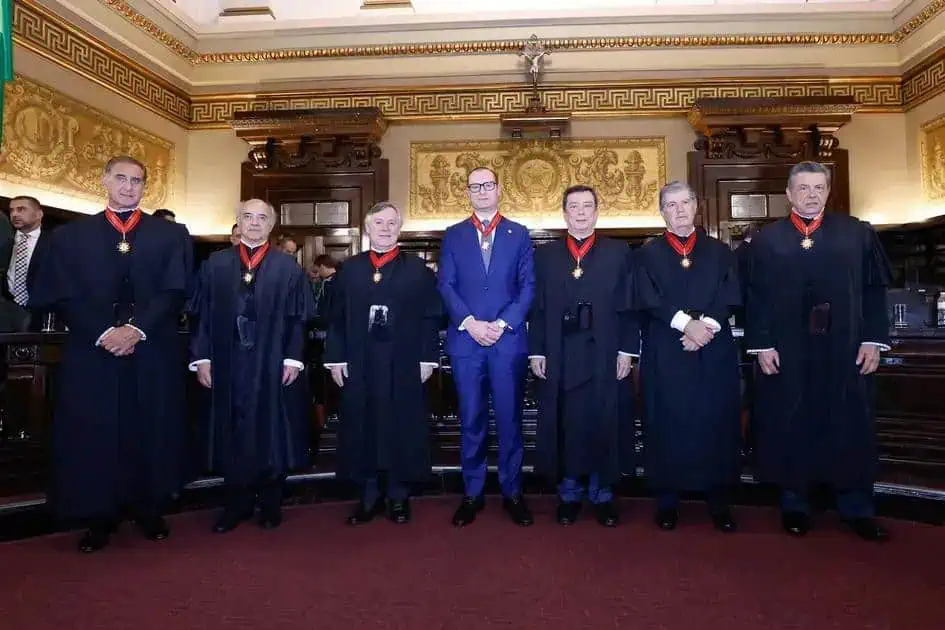 Juízes e autoridades em sessão do tribunal de justiça com decoração clássica e símbolos de poder jurídico.