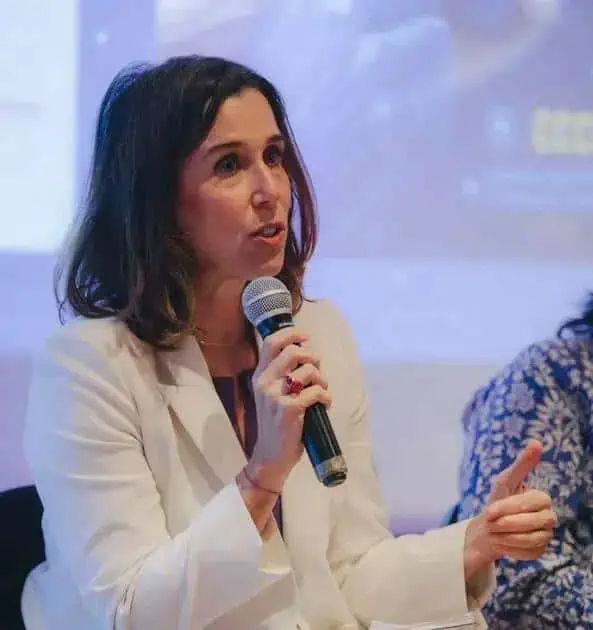 Advogada falando em evento jurídico com microfone, ambiente profissional, woman com expressão séria, discutindo temas de direito, destaque em notícias jurídicas, evento de direito hoje.
