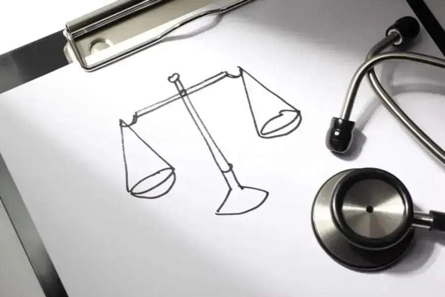 Ícone de balança de justiça desenhada em papel com estetoscópio ao lado, simbolizando o direito e a área da saúde.