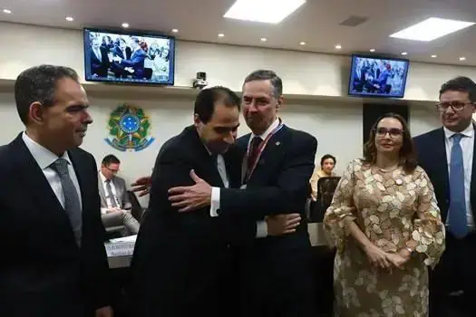 Profissionais do direito em reunião oficial, troca de cumprimentos e networking no ambiente de uma sala de tribunais ou conferências, com telas exibindo imagens institucionais ao fundo.