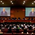 Profissionais em conferência de direito, com a tela exibindo um convidado e o público atento ao evento jurídico.