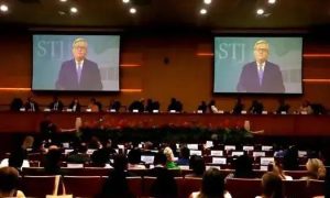 Profissionais em conferência de direito, com a tela exibindo um convidado e o público atento ao evento jurídico.